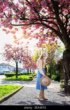 Donna nel parco sotto i fiori di ciliegio, vivace scena primaverile e ispirazione per i viaggi. Foto Stock