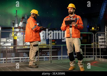Esperti di piattaforme marittime offshore che utilizzano tablet per analizzare l'efficienza di estrazione durante le 24 ore di funzionamento. Equipaggio del carro di perforazione che configura i sistemi di gestione delle navi con il dispositivo a tarda notte Foto Stock