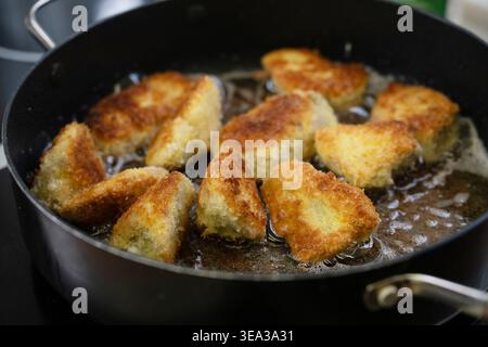 Friggendo pezzi di carne o pesce impanati in olio caldo in una padella nera, diventano ancora più croccanti grazie al pangrattato panko giapponese, alla messa a fuoco selezionata, stretto Foto Stock