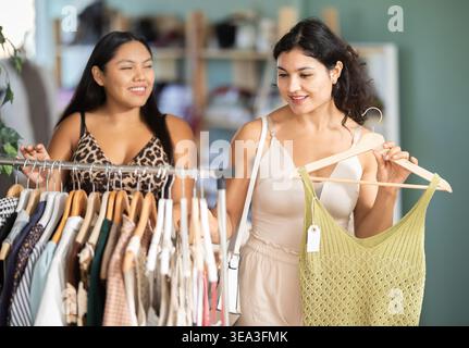 Due giovani donne che scelgono abiti estivi o top in un negozio di abbigliamento Foto Stock