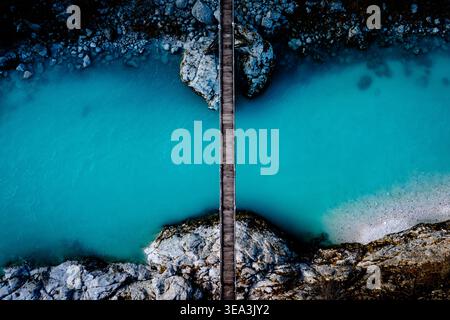 Vista aerea di una stretta passerella in legno che attraversa un vivace fiume turchese con sponde rocciose e acque cristalline in Slovenia. Foto Stock