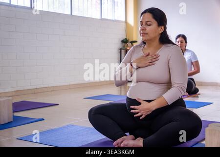 Donna incinta che pratica meditazione sulla consapevolezza, mettendo le mani sul petto e sulla pancia per respirare calmante Foto Stock