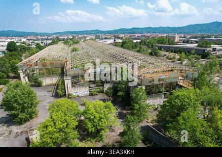 Veduta aerea di un sito industriale abbandonato con tetti scheletrici e vegetazione sovrastata a Settimo Torinese, Piemonte, Italia. Foto Stock