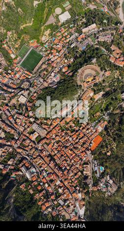 Vista aerea dell'Antico Teatro di Taormina circondato da storici tetti in terracotta e lussureggianti colline verdi a Taormina, Sicilia, Italia. Foto Stock