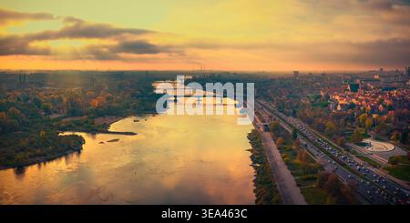 Vista aerea del fiume Vistola che scorre attraverso la città con ponti storici e alberi autunnali durante un tramonto dorato Varsavia, voivodato della Masovia, Foto Stock