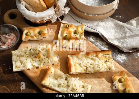 Fette di focaccia italiana artigianale con olive e cipolle su tavola di legno con tradizionale setaccio di farina. Lo scatto ad angolo alto offre una varietà di riprese fatte in casa Foto Stock