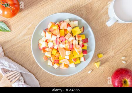Un primo piano di insalata di frutta e verdura fresca in una ciotola con pomodoro, mela e una tazza di latte su un piatto di legno. Vista dall'alto. Posizione piatta. Foto Stock