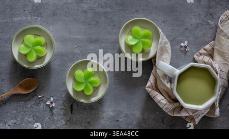 Vista dall'alto di una torta di panda al vapore su piccole tazze, servita con una tazza di tè verde, un tradizionale dessert tailandese. Primo piano. Posizione piatta. Foto Stock