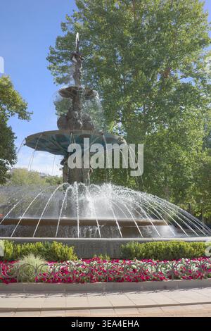 Fontana in bronzo ornata a gradini con acqua a cascata e sculture femminili, circondata da vivaci aiuole di fiori rossi e bianchi in un giardino pubblico, Granada Foto Stock