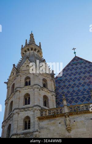 La torre della cattedrale di Santo Stefano e i dettagli del tetto piastrellato a motivi geometrici visti dal basso contro il cielo azzurro a Vienna, Austria. Foto Stock