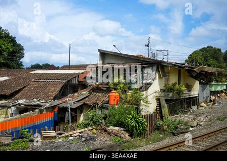 Una vista delle case improvvisate e degli affollati insediamenti urbani costruiti pericolosamente vicino a una linea ferroviaria sotto un cielo blu. La scena raffigura la povertà urbana A. Foto Stock