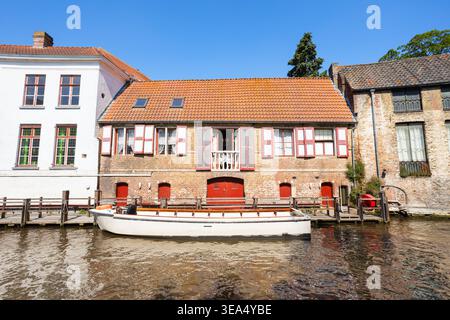 Casa tradizionale sul canale con persiane rosse e barca turistica nella città di Bruges, Paesi Bassi Foto Stock