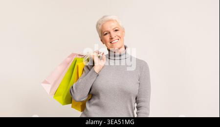 Donna matura che sorride mentre tiene in mano borse colorate in un moderno spazio interno Foto Stock