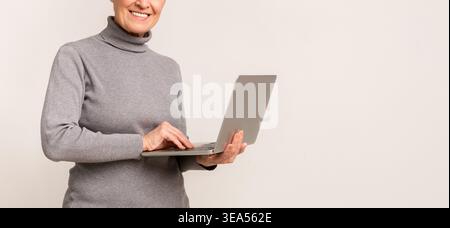 Donna anziana che utilizza un notebook in un ambiente informale sorridendo e divertendosi Foto Stock