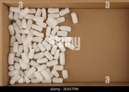 Polistirolo che impacchettano le arachidi su sfondo di scatola di cartone. Pellet in schiuma di plastica bianca protettivi per l'imballaggio dei pacchi. Foto Stock