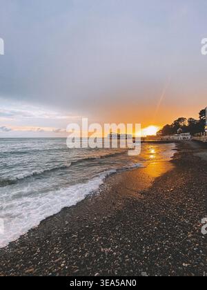 Tramonto dorato sul mare con profilo del molo e onde sulla spiaggia di ciottoli Foto Stock