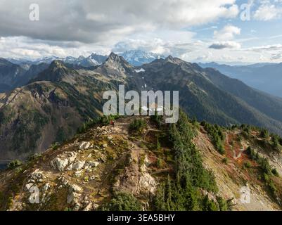 Vista aerea del Winchester Mountain Lookout su un picco accidentato con escursionisti nelle vicinanze e le catene montuose circostanti sotto un cielo nuvoloso nella contea di Whatcom, W Foto Stock