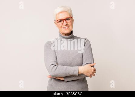La donna sorridente che indossa gli occhiali si pone con sicurezza contro uno sfondo neutro Foto Stock