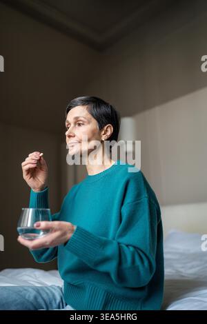Donna anziana che assume una medicina speciale per curare la malattia, donna anziana con malattia che tiene un bicchiere d'acqua e un integratore di pillole, trattamento sanitario per anziani, farmacologia e prevenzione delle malattie. Foto Stock