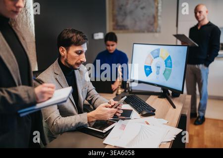 Team aziendale che collabora in un ufficio moderno con manager utilizzando smartphone e monitor Foto Stock