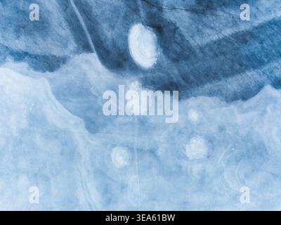 Vista aerea del lago di Charpal ghiacciato con intricati motivi di ghiaccio e formazioni circolari bianche sulla superficie blu di Lozere, Occitanie, Fran Foto Stock