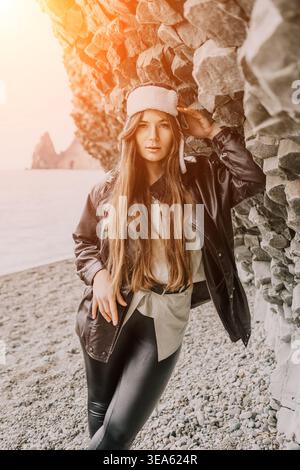 Donna spiaggia inverno ritratto di una bella giovane donna che indossa un cappello ushanka e una giacca di pelle vicino alle rocce di basalto sulla riva Foto Stock