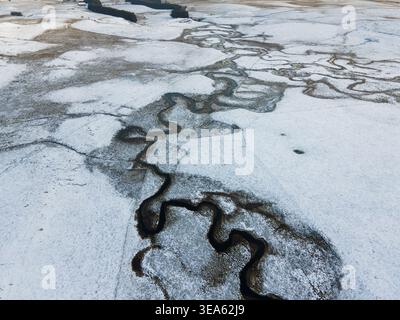 Vista aerea di un tortuoso fiume che scorre attraverso campi innevati e paesaggi rurali invernali a Nasbinals, Occitanie, Francia. Foto Stock
