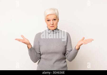 La donna matura esprime confusione mentre gesti con le mani in posizione neutra Foto Stock