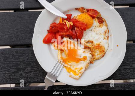 Uova fritte con pomodori ciliegini servite su un piatto bianco posto su un tavolo di legno scuro. Vista dall'alto. Copia spazio Foto Stock