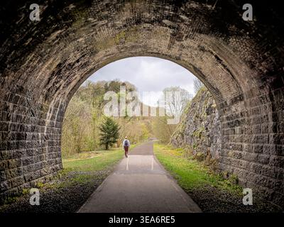 Veduta posteriore di una camminatrice che esce dal tunnel ferroviario in disuso sul Monsal Trail, Peak District National Park, Derbyshire, Inghilterra, Regno Unito Foto Stock