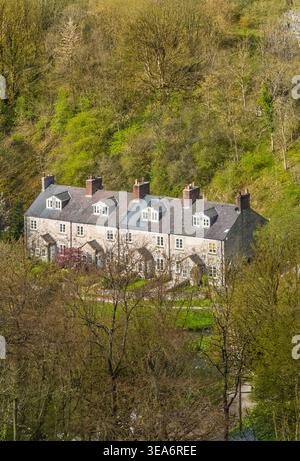 Blackwell Mill Cottages vista dal Monsal Trail nella Wye Valley, Peak District, Derbyshire, Inghilterra, circondato da boschi e vegetazione primaverile. Foto Stock