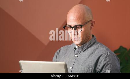 Uomo d'affari che lavora su un notebook in un ufficio moderno con occhiali che si concentrano sullo schermo Foto Stock