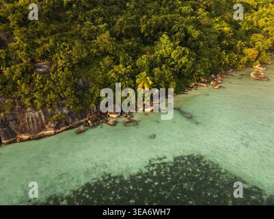 Vista aerea della lussureggiante foresta tropicale e dei massi di granito lungo la costa turchese di Cap Ternay, Port Glaud, Seychelles. Foto Stock