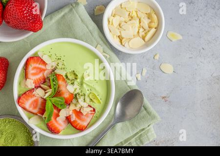 Ciotola di yogurt matcha con tè verde e fragole, menta e mandorle con cucchiaio su fondo grigio in cemento. Vista superiore con spazio di copia Foto Stock