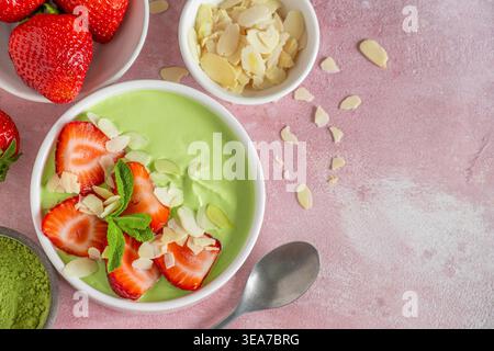 Cremoso yogurt verde matcha servito con fragole a fette e scaglie di mandorle in un recipiente con cucchiaio. Vista superiore con spazio di copia. Dessert sano, proteine Foto Stock