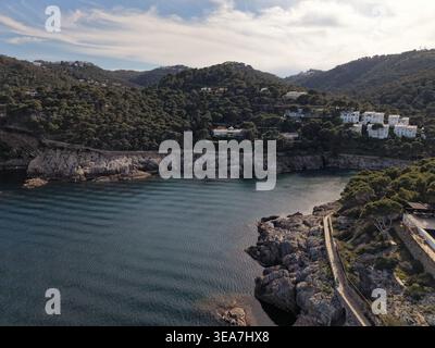 Immagine grandangolare della baia di Cala Aiguafreda che mostra la costa frastagliata, i fitti pini, le ville di lusso e il Mar Mediterraneo su un soleggiato su Foto Stock