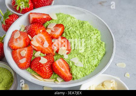 Budino di tè verde matcha chia con fragole fresche e fiocchi di mandorle in una ciotola di ceramica su sfondo grigio in cemento. Dessert salutare e vegetariano Foto Stock