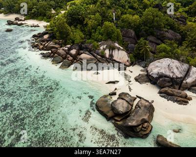 Vista aerea delle formazioni rocciose di granito e della spiaggia di sabbia bianca con acqua turchese e lussureggiante foresta tropicale a Takamaka, Seychelles. Foto Stock