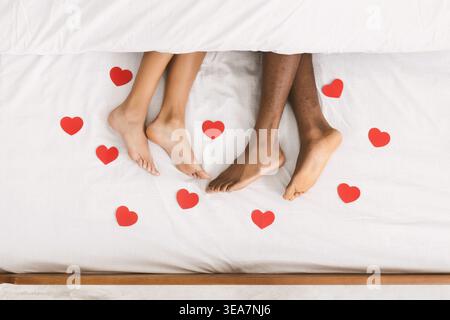 Amate le gambe di coppia sdraiate sul letto sotto la coperta Foto Stock