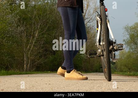 Ripresa ad angolo basso delle gambe dei ciclisti in piedi accanto a una bicicletta Foto Stock
