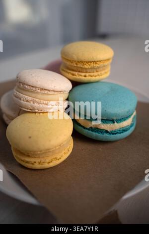 primo piano di colorati macaron francesi impilati su pergamena marrone con luce naturale soffusa, giallo pastello, blu, crema e rosa conchiglie con ripieno cremoso, Foto Stock