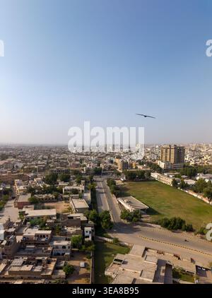 Vista aerea del paesaggio urbano con fitti edifici residenziali, un'ampia strada e un parco verde sotto un cielo azzurro a Hyderabad, Sindh, Pakista Foto Stock