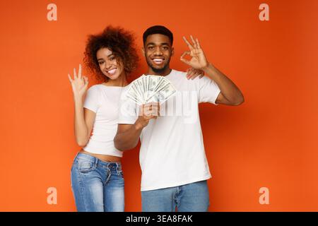 Allegra coppia afro-americana che mostra segni buoni con un mucchio di soldi Foto Stock