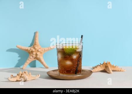 Bicchiere di cocktail Cuba Libre freddo con stelle marine su tavolo bianco su sfondo blu Foto Stock