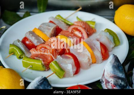 Spiedini di pesce e verdura animati disposti su bastoncini pronti per l'evento di grigliatura estivo Foto Stock