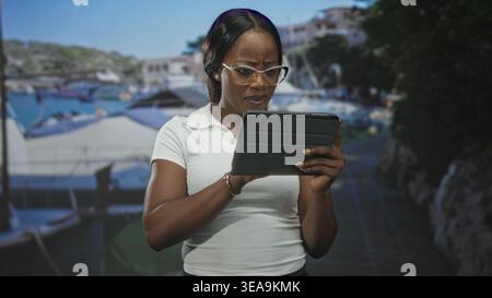 Donna che tiene in mano un tablet e sta girovagando mentre legge con le dita sullo schermo in uno studio con sfondo porticciolo e oggetti di scena del molo; attenzione all'esame. Foto Stock