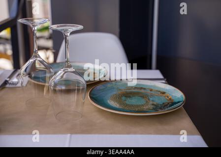 Primo piano di un tavolo del ristorante con piatti e bicchieri da vino capovolti in luce naturale con un delicato sfondo sfocato. Foto Stock