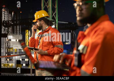 Team della piattaforma di estrazione del petrolio offshore che utilizza un computer portatile per controllare i sistemi sottomarini a tarda notte. Esperti che lavorano insieme per monitorare il rilevamento delle anomalie utilizzando un notebook sulla perforazione derrick Foto Stock
