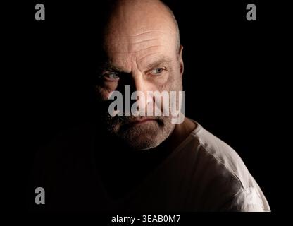 Ritratto dell'uomo calvo con ombre forti che mettono in risalto un'espressione seria e occhi blu Foto Stock