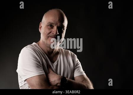 Uomo sorridente che si sente sicuro di sé, posa in studio con illuminazione a chiave bassa Foto Stock
